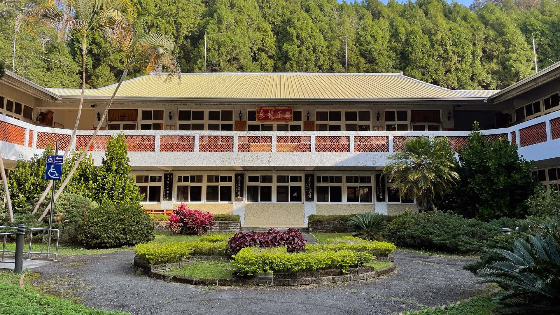 天人研究總院正面外觀：兩層樓傳統中式金頂建築，正面掛有紅底金字匾額，匾額書「參機正殿」，前有圓形灌木花圃，四周環繞棕櫚與熱帶樹木，背倚翠綠山林